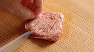まな板の上の牛たんに包丁を入れる手元