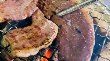 炭火の網の上で焼いている厚切りのハツをトングでつかんだところ