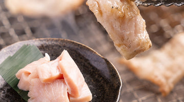 黒い皿に盛った生のミノと、焼き網の上でトングにはさんだ焼き色のついたミノ