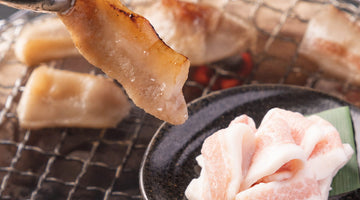 黒い皿に盛った生の豚トロと、焼き網の上でトングにはさんだ焼き上がりの豚トロ