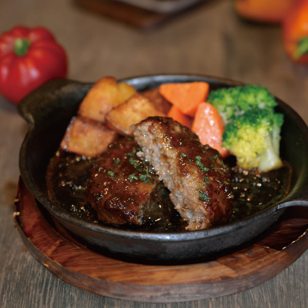 牛たんハンバーグセットの画像。ジューシーな牛たんハンバーグが黒い鉄板に盛り付けられ、付け合わせにポテト、ニンジン、ブロッコリーが添えられています。