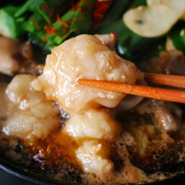 国産牛もつ鍋セットの具材を箸で持ち上げている様子。ぷりぷりした牛もつと新鮮な野菜が盛り付けられた鍋の一部で、家庭で楽しむための2~3人前のボリューム感が伝わる。