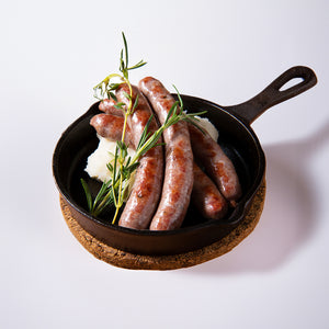 訳あり牛たんソーセージがフライパンに盛り付けられた画像。ジューシーなソーセージが数本、ハーブと共に白いマッシュポテトの上に置かれています。