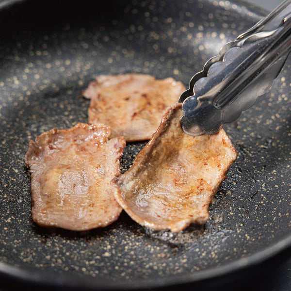 薄切り牛たんの焼肉用がフライパンで焼かれている様子。色は淡い茶色で、ジューシーな肉質が特徴。焼き目がついて香ばしさが引き立つ。