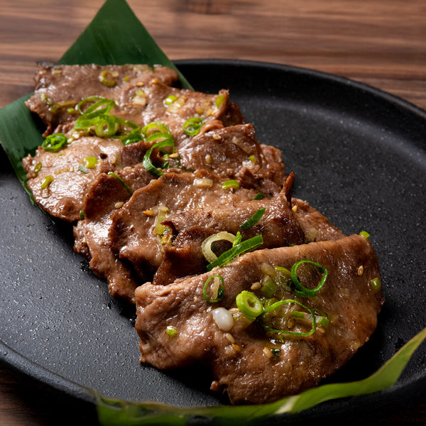 焼肉用の薄切り牛たんが盛り付けられた黒い皿。香味ネギがトッピングされ、ジューシーな肉質が特徴的。